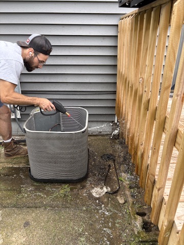 Technician rinsing and cleaning the coil fins on an outdoor condenser unit at a Niles, MI area home