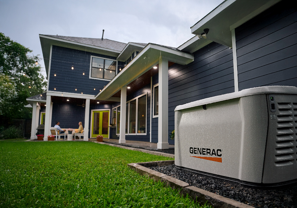 A Generac home standby generator installed on a pad beside a modern home at dusk