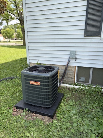 A Goodman AC condenser installed on a pad in a backyard beside a home in the Niles, MI area